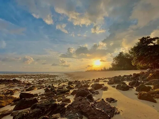 Ein felsiger Strand, beleuchtet von einem goldenen Sonnenuntergang unter bewölktem Himmel.