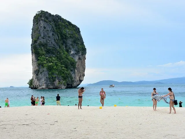 Touristen genießen einen weißen Sandstrand mit einer markanten Kalksteinformation in der Nähe.