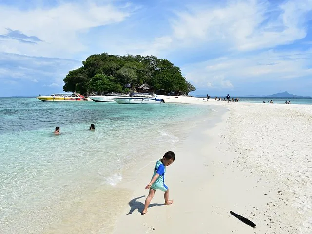 Ein kleiner Junge läuft an einem weißen Sandstrand in der Nähe von Speedbooten entlang.