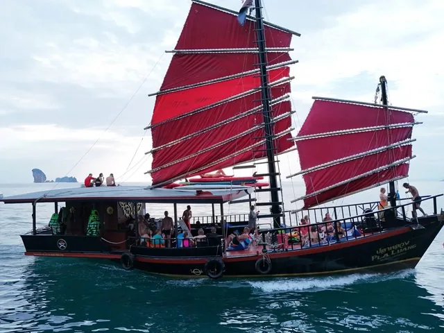 Ein traditionelles Dschunkenboot mit roten Segeln, das im Meer vor Anker liegt.