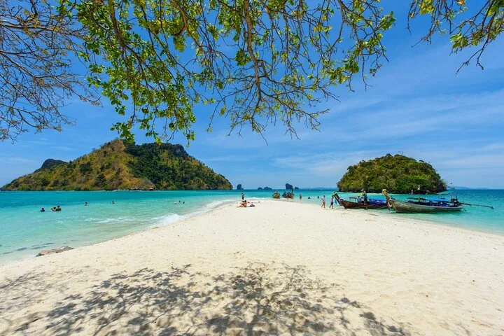 Eine lange Sandbank, die türkisfarbene Wasserbereiche trennt und mit einer üppigen, felsigen Insel verbunden ist.