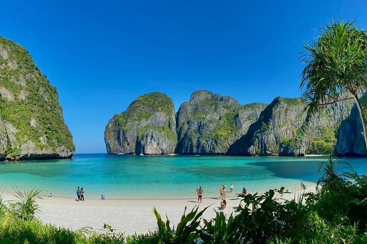 Touristen entspannen an einem makellosen weißen Sandstrand, umgeben von hoch aufragenden Kalksteinfelsen.
