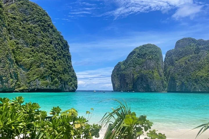 View from the beach towards towering limestone cliffs enclosing a vibrant turquoise bay.