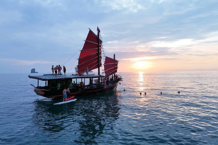 Ein traditionelles Dschunkenboot mit roten Segeln, das sich vor einem wunderschönen Sonnenuntergang abzeichnet.